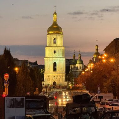 Beleuchteter Kirchturm und Straßenverkehr im abendlichen Stadtbild von Kiew